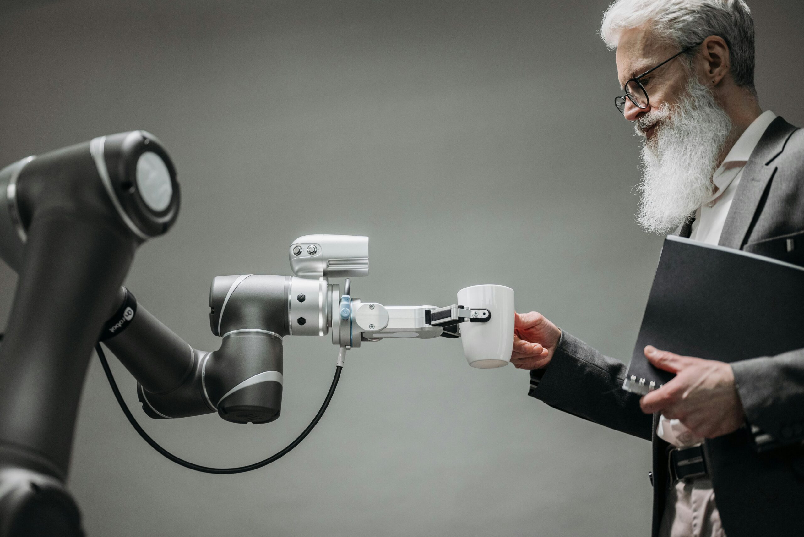 Robot arm handing a coffee mug to a professional businessman symbolizing AI and human collaboration